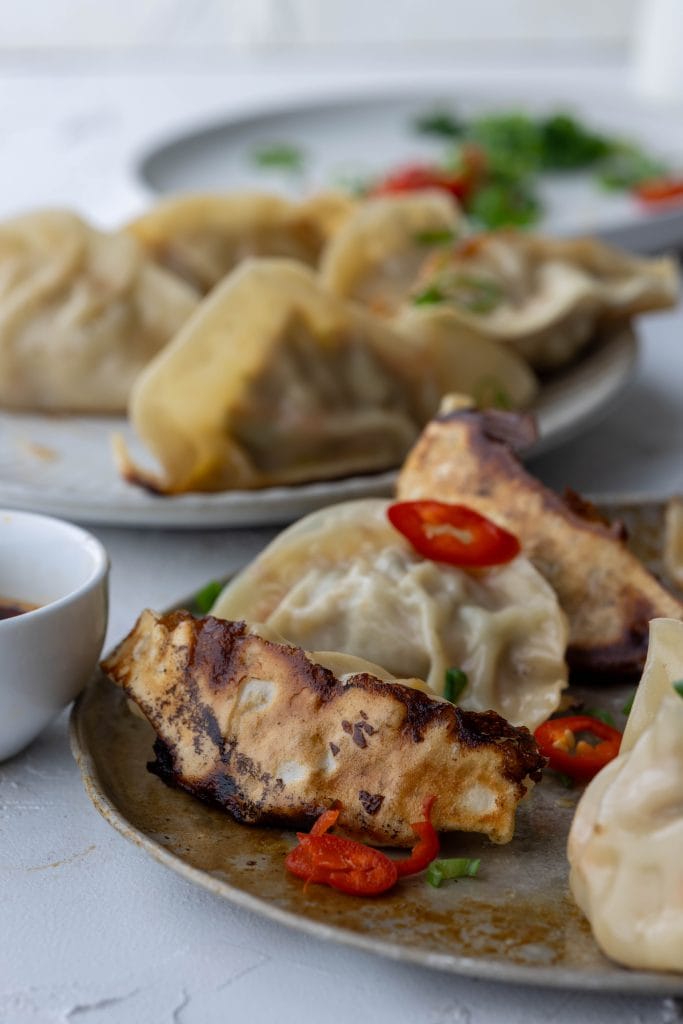 plates of dumplings with small bowl of dipping sauce and garnishes