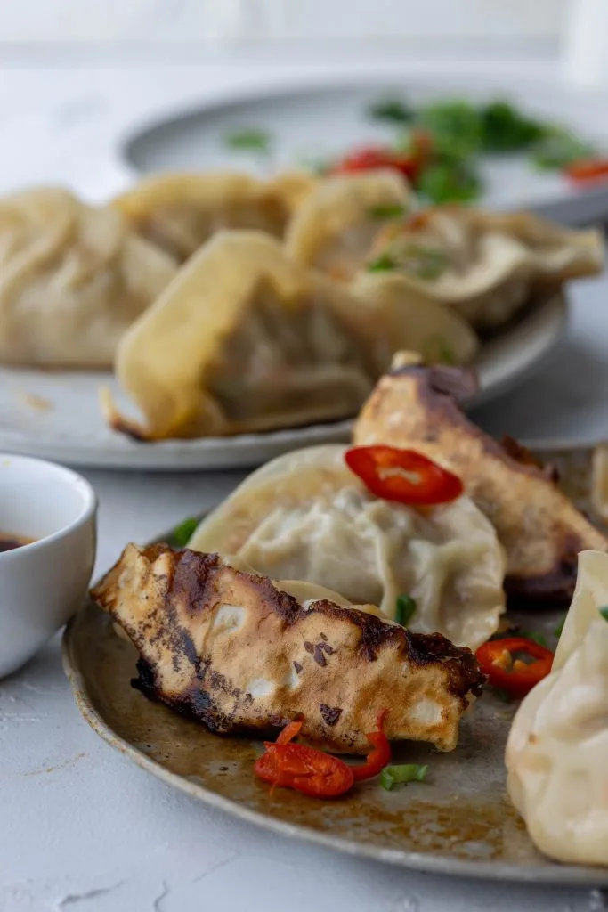 plates of dumplings with small bowl of dipping sauce and garnishes