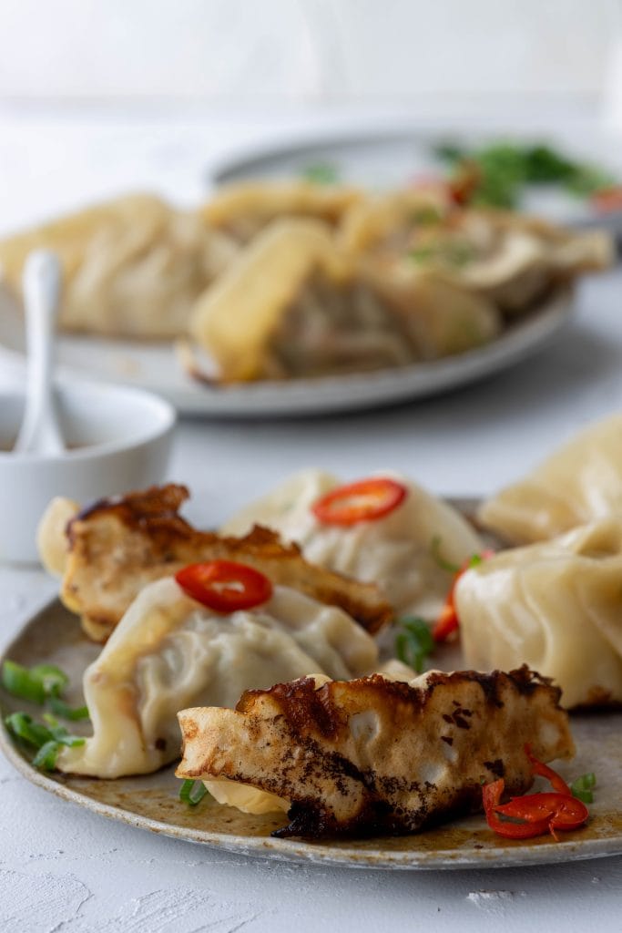 White plate of stacked gyoza pan fried dumplings garnished with chilli and coriander