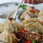 hand drizzling soy sauce over plate of dumplings