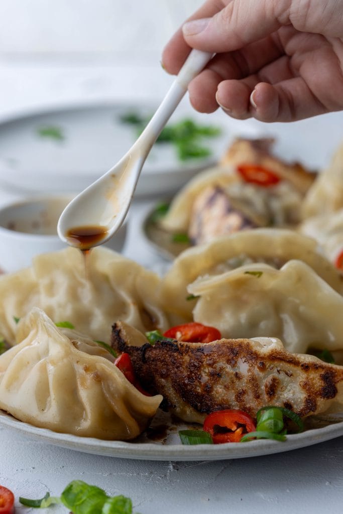 hand drizzling soy sauce over plate of dumplings