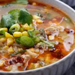Close up of chicken & corn soup in light grey bowl garnished with coriander.