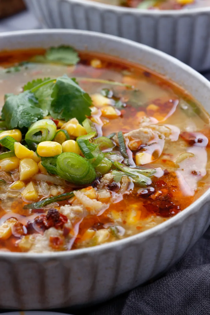 Close up of chicken & corn soup in light grey bowl garnished with coriander.