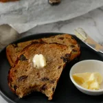 Slices of buttered raisin toast with bite mark. Sitting on grey plate.