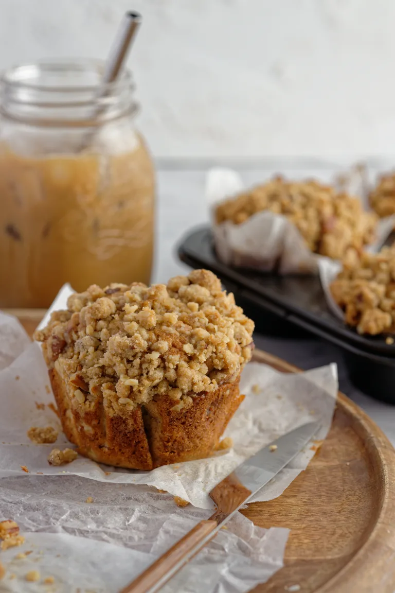 muffin on baking paper with jar of iced coffee and muffins in background.