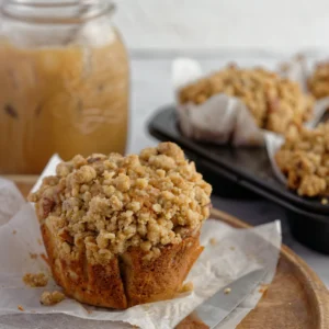 muffin on baking paper with jar of iced coffee and muffins in background.