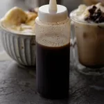 Clear bottle with chai syrup. Chai coffee and hot chocolate in background.