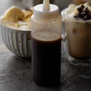 Clear bottle with chai syrup. Chai coffee and hot chocolate in background.