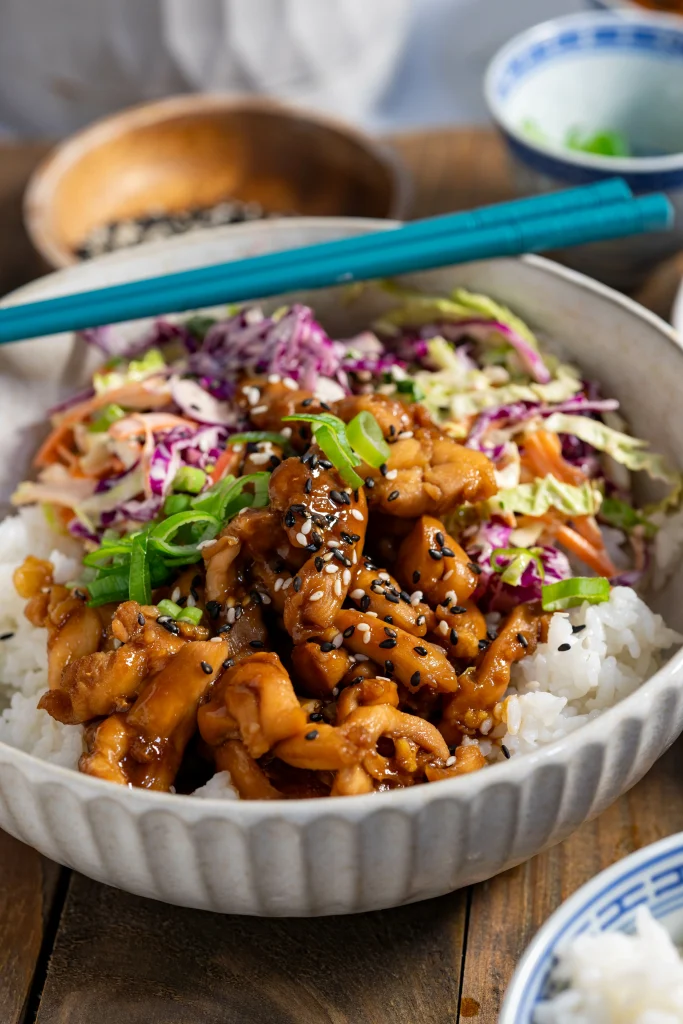 Grey Bowl of sushi rice, Marinated cooked chicken with slaw. Chopsticks resting on bowl