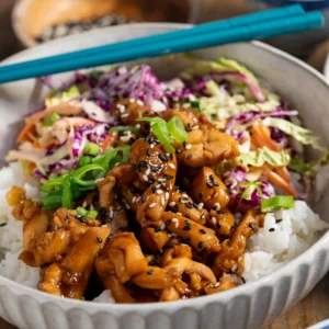 Grey Bowl of sushi rice, Marinated cooked chicken with slaw. Chopsticks resting on bowl