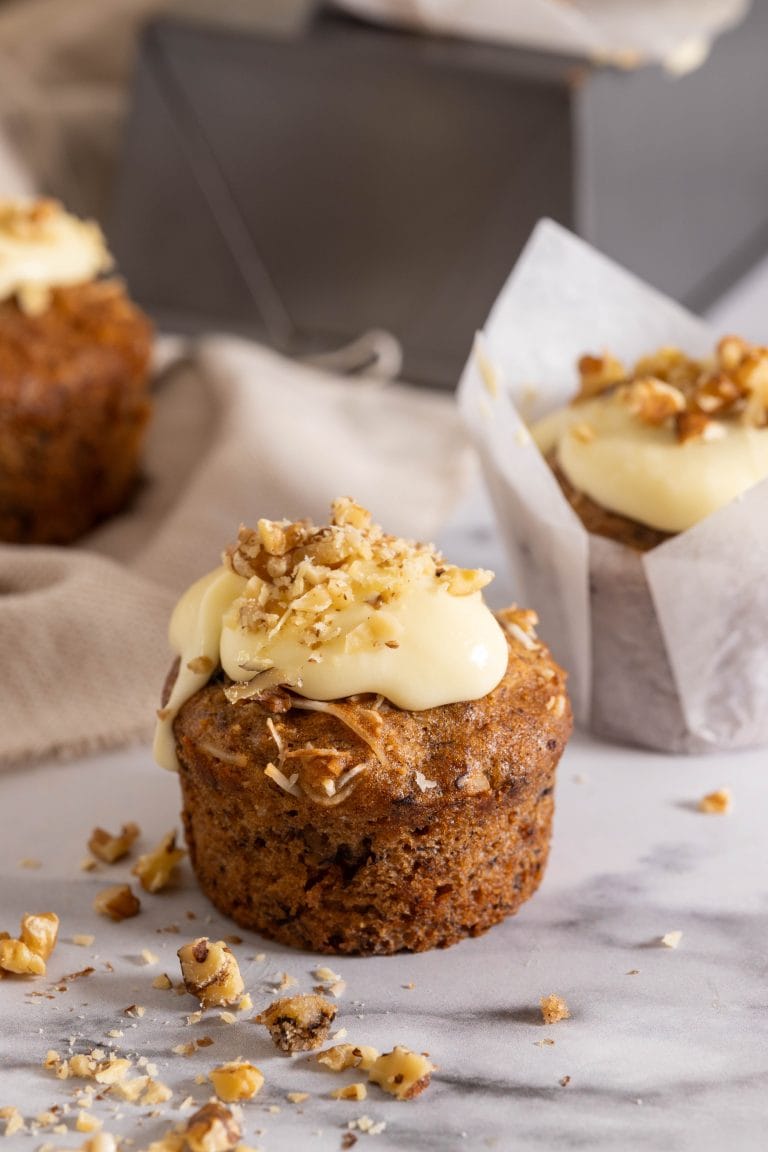 Spiced pineapple banana cupcake topped with frosting and topped with chopped walnuts