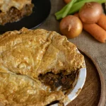 Beef pie topped with flakey puff pastry surrounded by ingredients used ot make it
